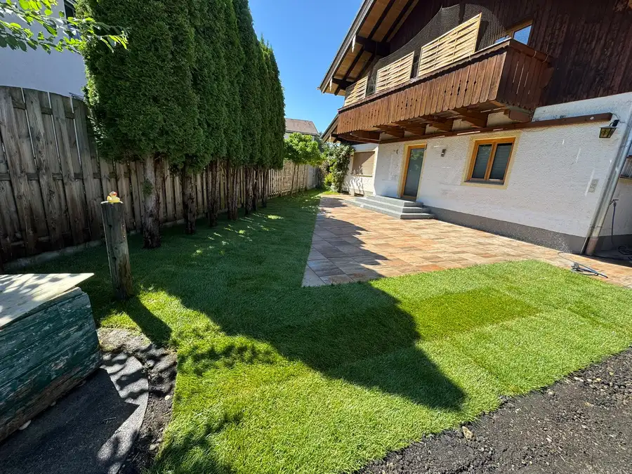 Derselbe Garten fertig: neue Natursteinterrasse und frischer Rollrasen