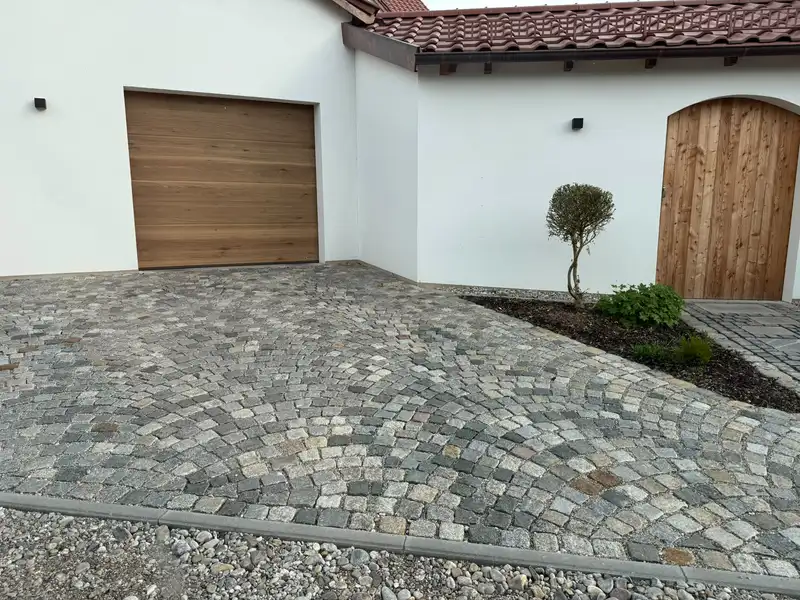 Einfahrt aus Kopfsteinpflaster vor einem Haus mit Holztor