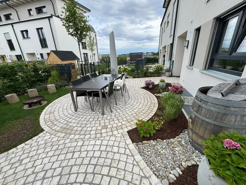 Runder Sitzplatz aus Kleinpflaster mit Esstisch und Beet