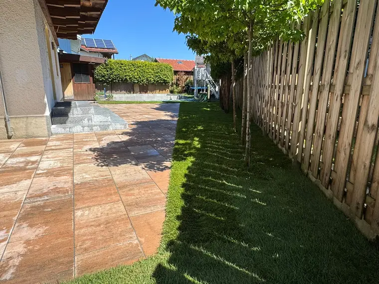 Gepflasterte Terasse mit Rasenstreifen und Holzzaun im Garten