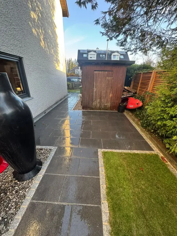 Gepflasterter Gartenweg neben Wohnhaus und hölzerner Gartenhütte