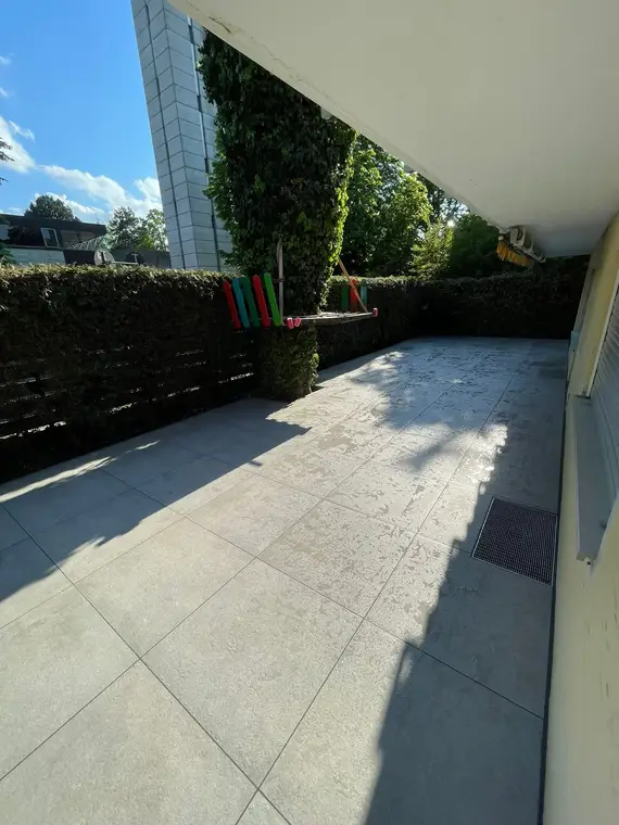 Gepflasterte Terrasse mit bunter Kinderschaukel und Hecke