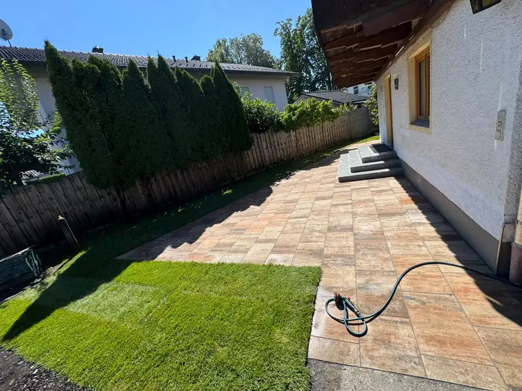 Gepflasterte Terrasse mit neuem Rasen und Gartenschlauch