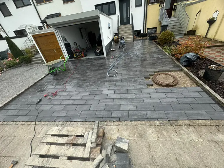 Gepflasterte Einfahrt mit Garage, Schubkarre und Baustellengeräten