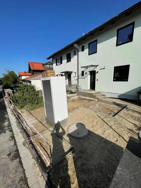Außeneinheit einer Wärmepumpe vor Wohnhaus mit Baustelle