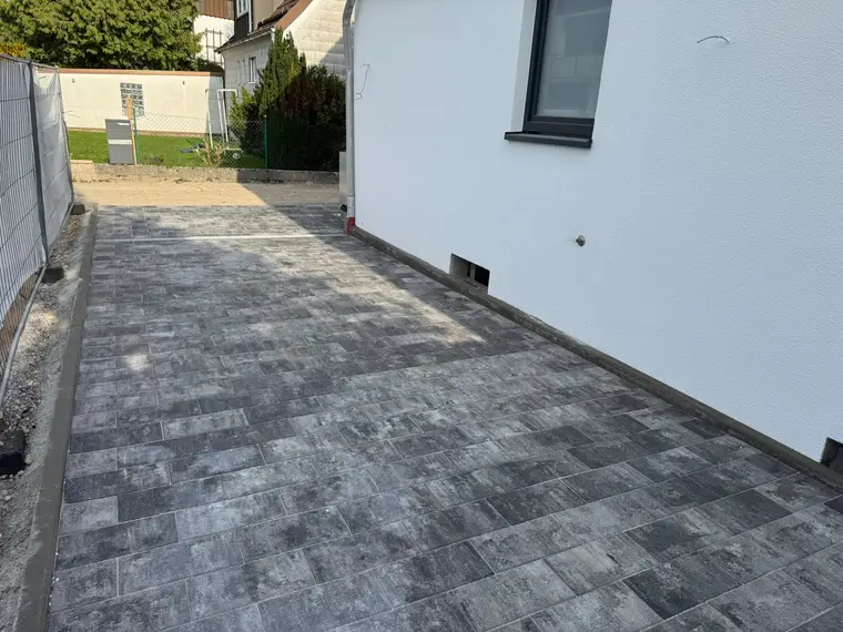 Frisch gepflasterte Hofeinfahrt an einer weißen Hauswand
