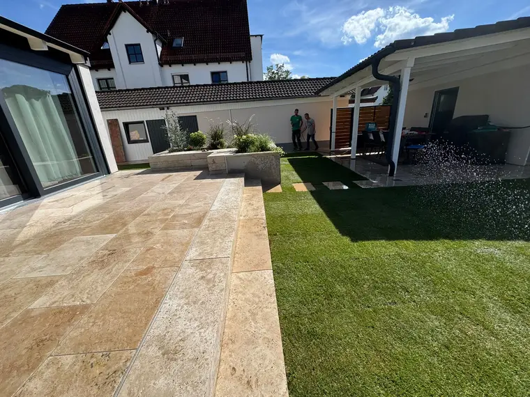 Gefliester Gartenbereich mit Rasen, Terrasse und zwei Personen im Hintergrund