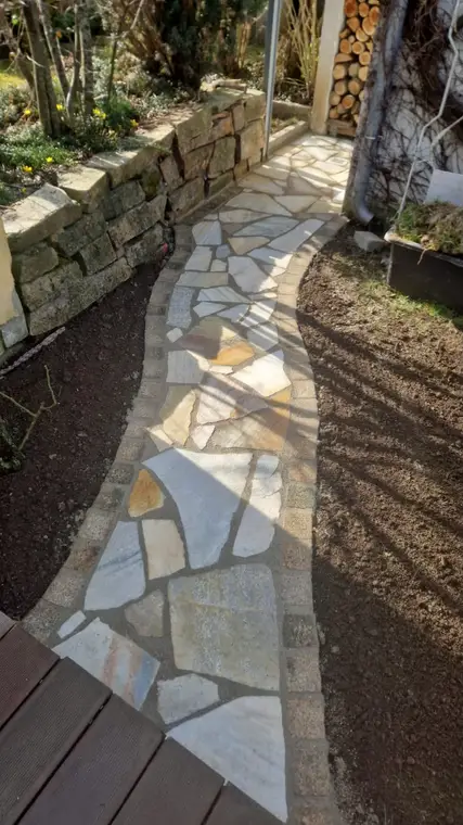 Gepflasterter Gartenweg aus Natursteinplatten zwischen Beeten