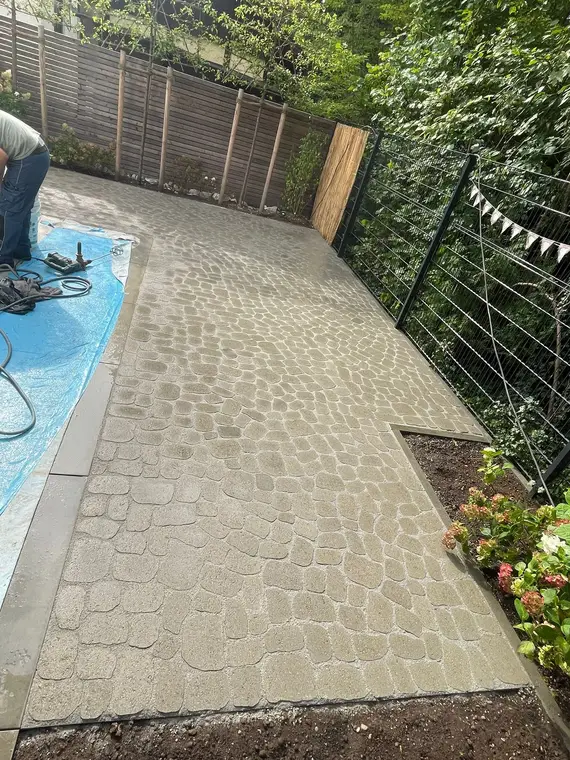 Gepflasterte Terrasse mit Zaun und Handwerker bei Pflasterarbeiten