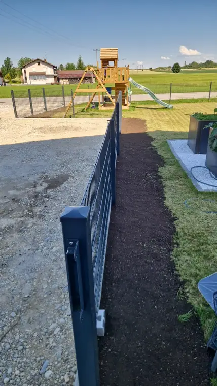 Neuer Metallzaun entlang eines Grundstücks mit Spielturm im Hintergrund