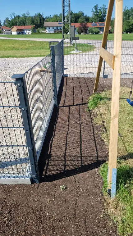 Frisch präparierter Erdstreifen entlang eines Metallzauns im Garten