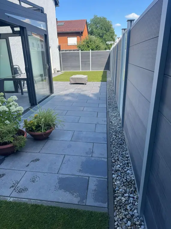 Terrasse mit Graumuster-Platten, Sichtschutzzaun und kleinem Rasenstück