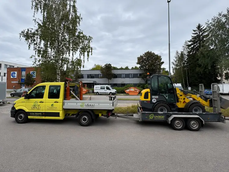 Gelber Transporter mit Unikat Gartenbau-Beschriftung und Radlader auf Anhänger