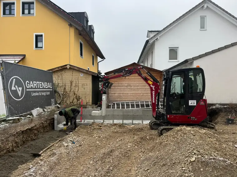 Minibagger setzt L-Steine an einer Baustelle im Garten