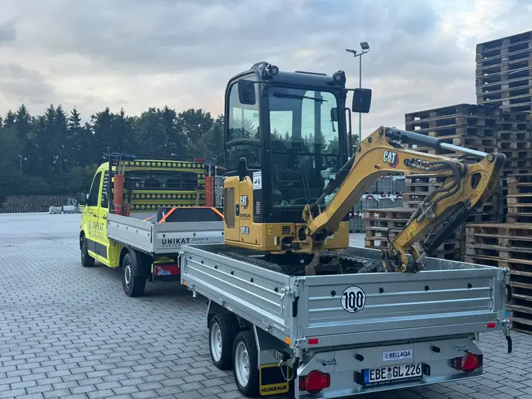 Gelber CAT-Minibagger auf Pkw-Anhänger vor UNIKAT-Pritschenwagen